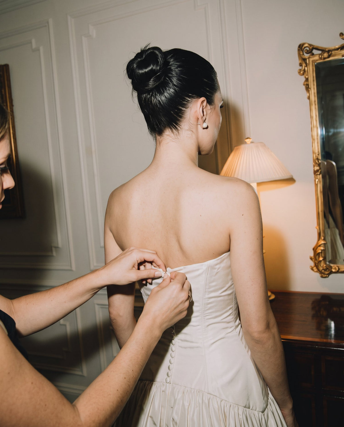 Mani che allacciano i bottoni sulla schiena della sposa