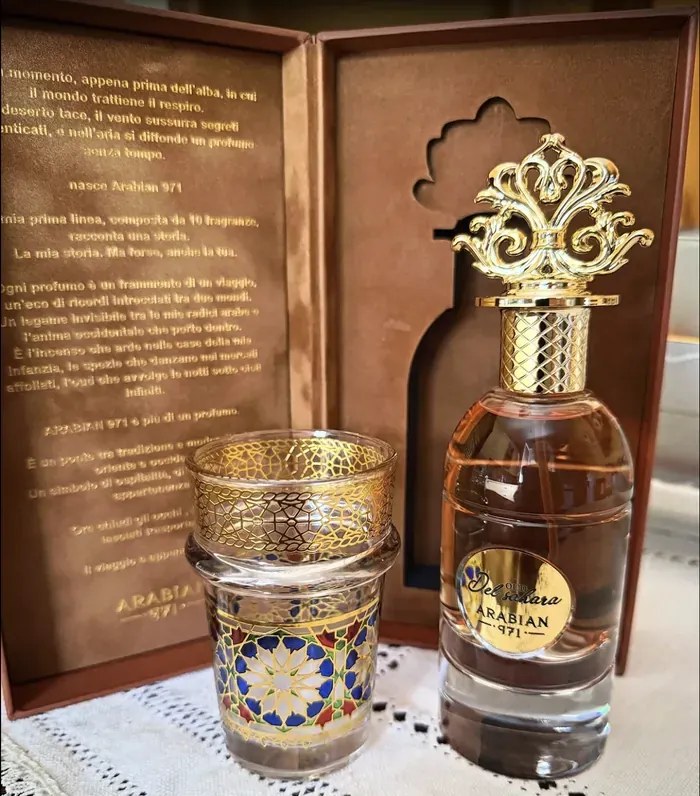 Oud El Sahara accanto a un bicchiere marocchino decorato, davanti al cofanetto marrone aperto.